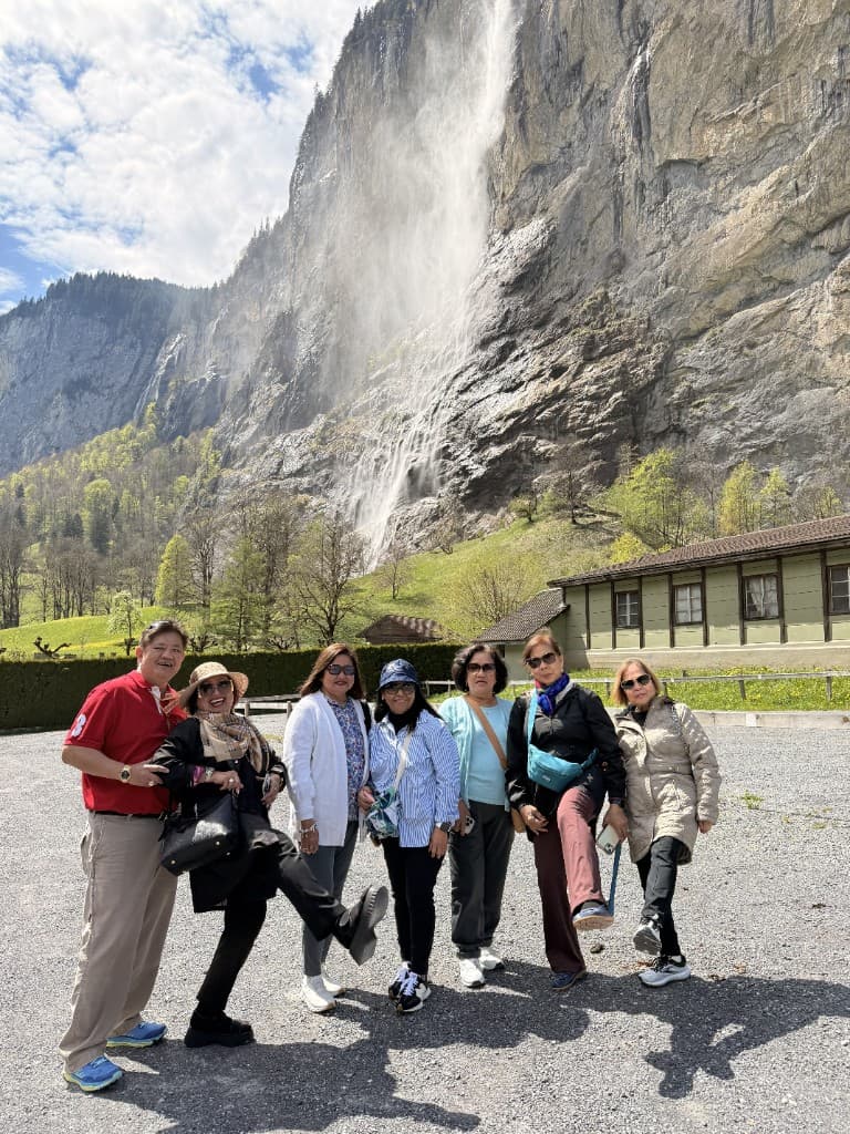 Group of travelers posing in front of a cliff and waterfall